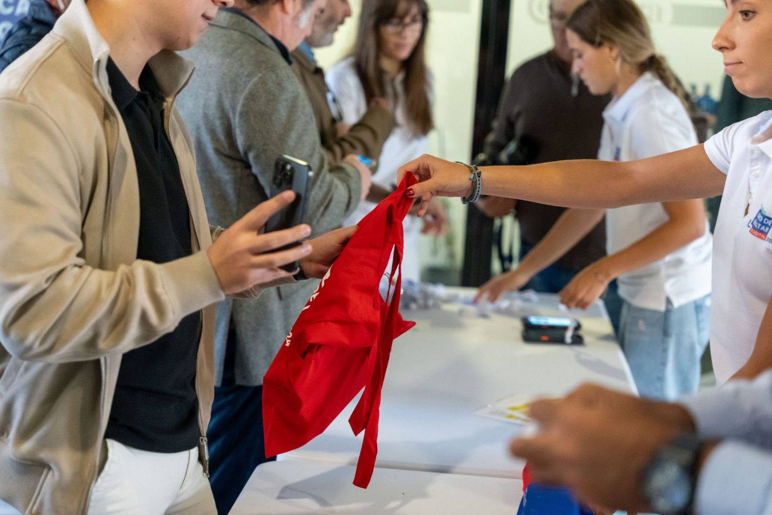 Voluntaria entregando una bolsa promocional del evento III Feria de Innovación 2025 a un asistente